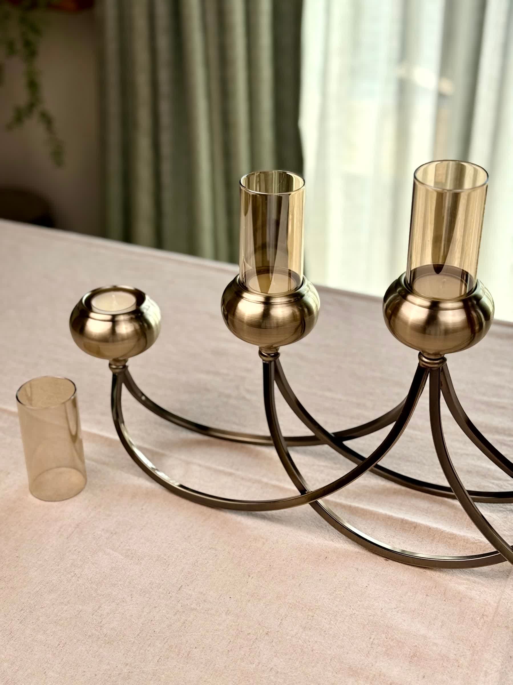 High Objects Aria Five-Arm Candle Stand with amber glass holders and antique brass finish. Sculptural metal design.
