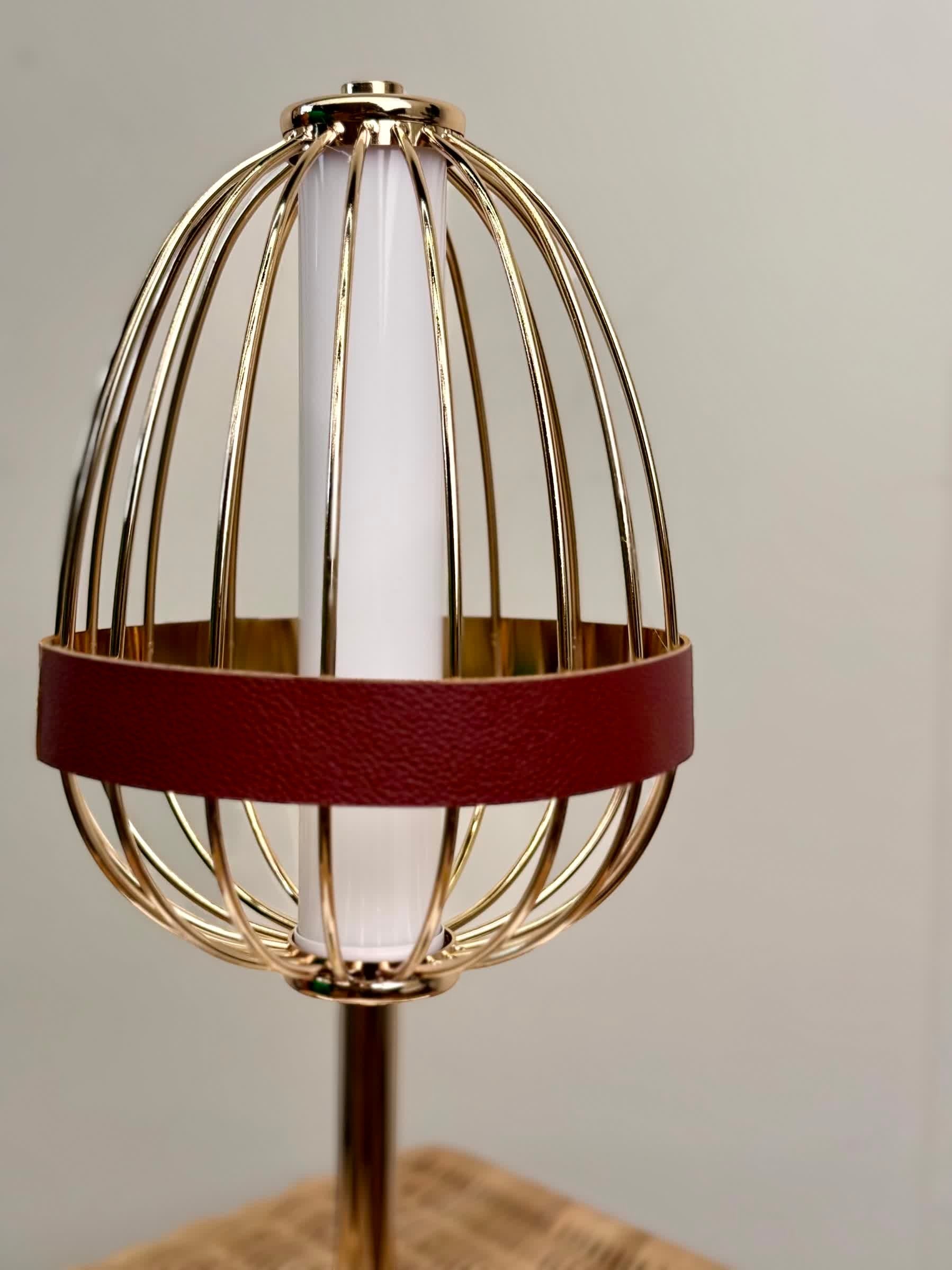 High Objects Aurette Cage Table Lamp with gold wire cage, white cylinder shade, and burgundy leather accent band.