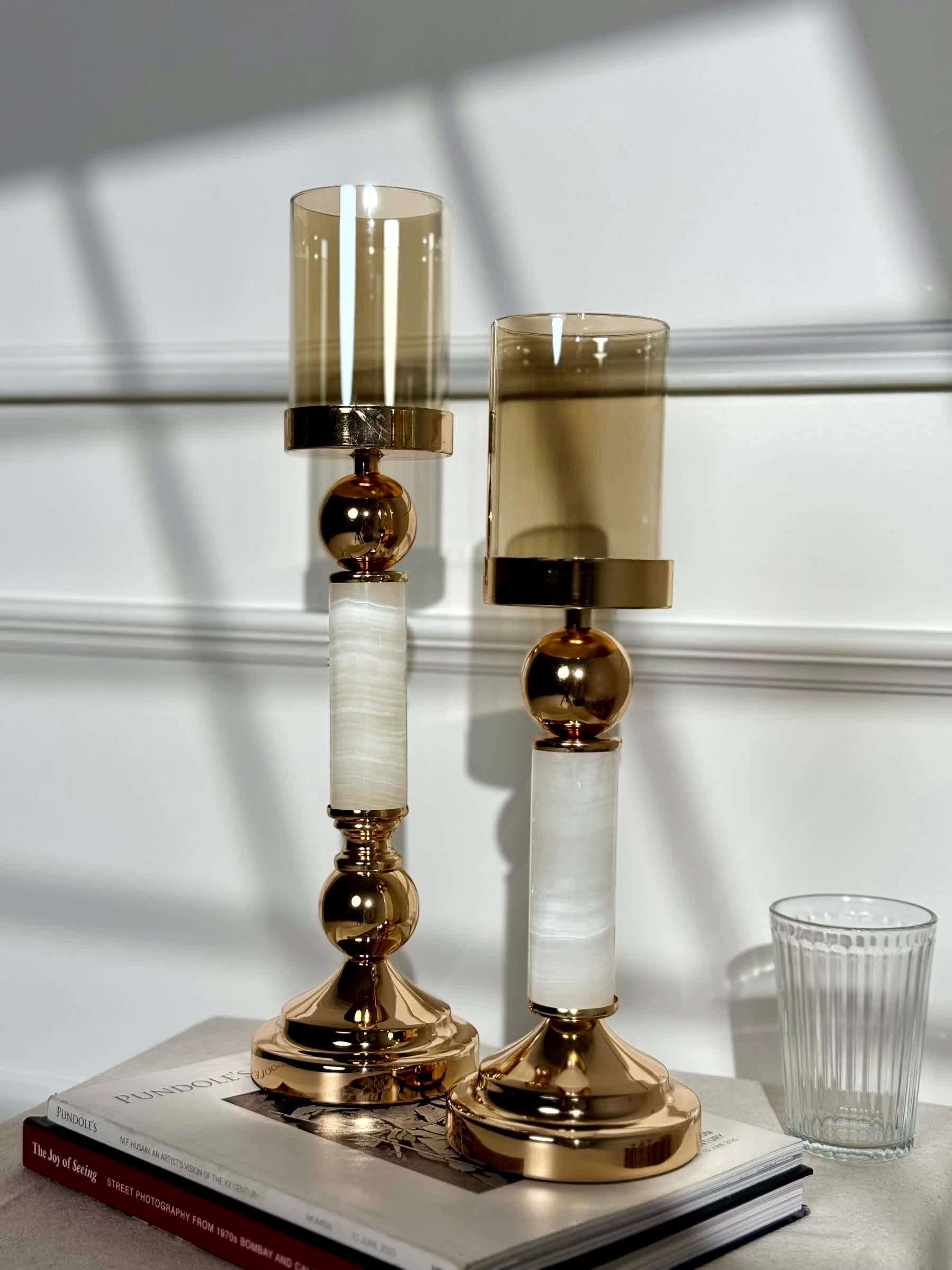 High Objects Aurora Column Candle Stand Set with amber glass shades and gold accents on white marble-inspired columns.