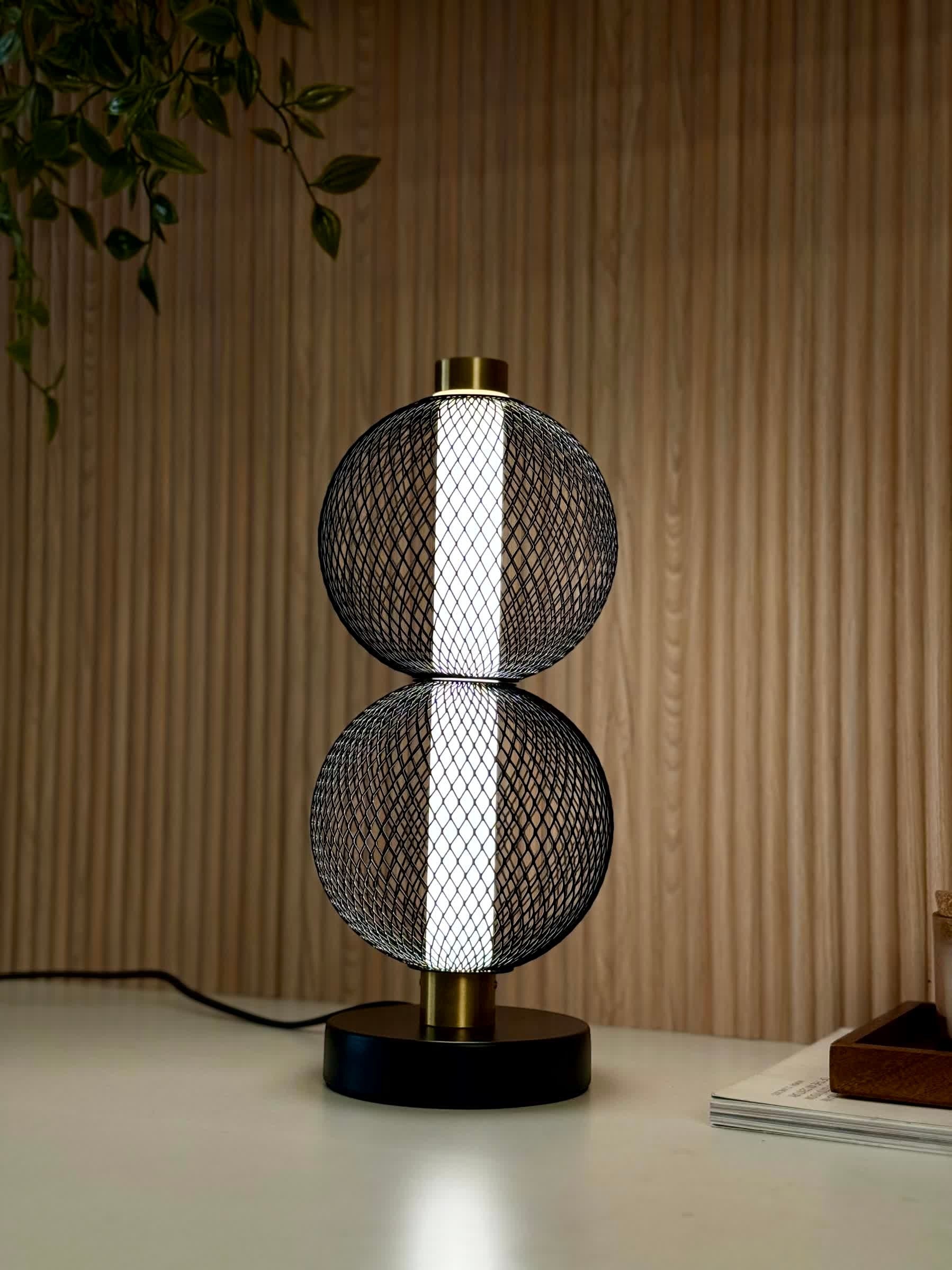 High Objects Celeste Duo Mesh Table Lamp with stacked spherical black mesh shades and brushed gold accents on a black base.
