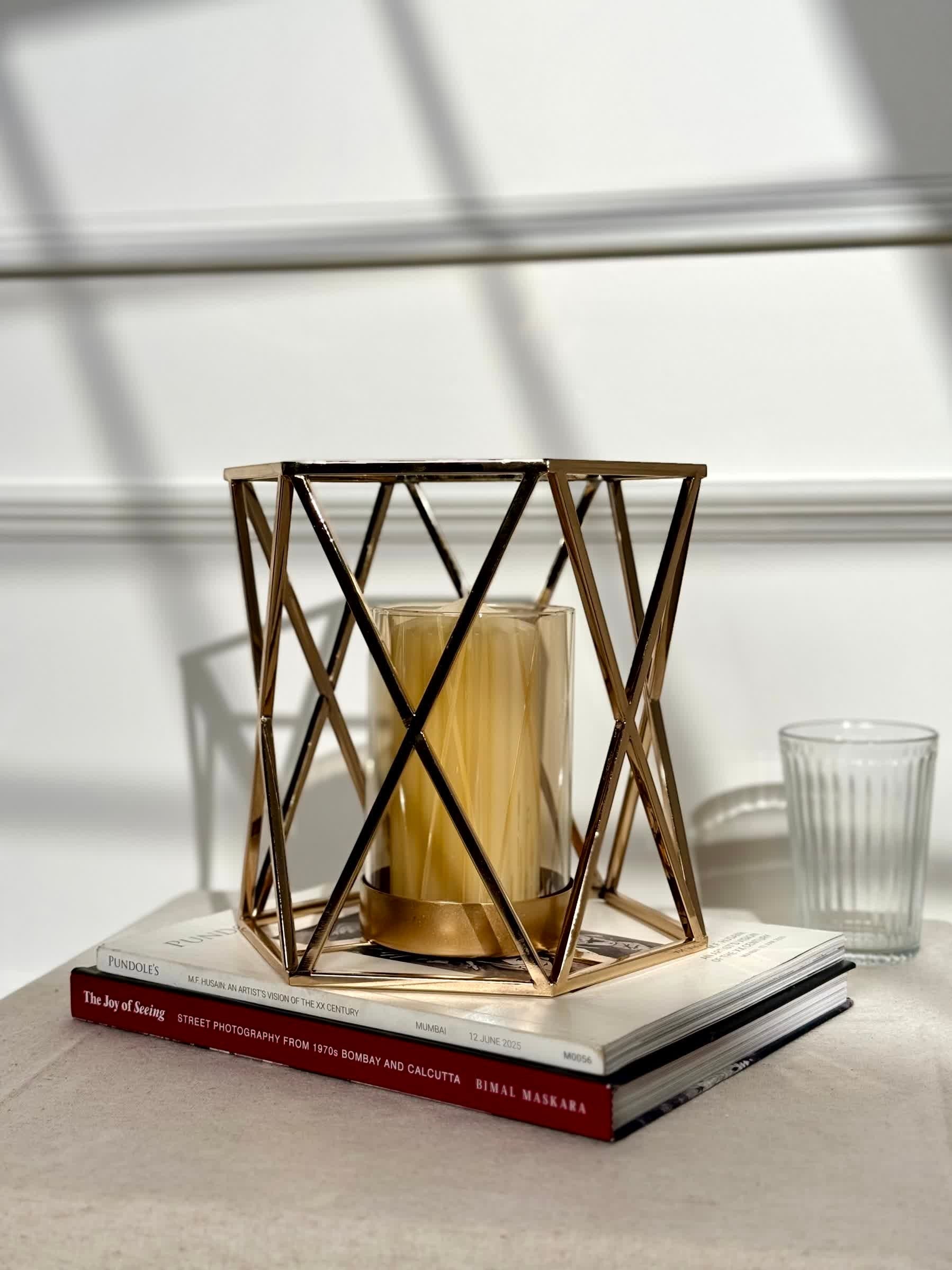High Objects Gilded Prism Candle Stand with gold geometric frame and glass holder, holding a yellow candle.