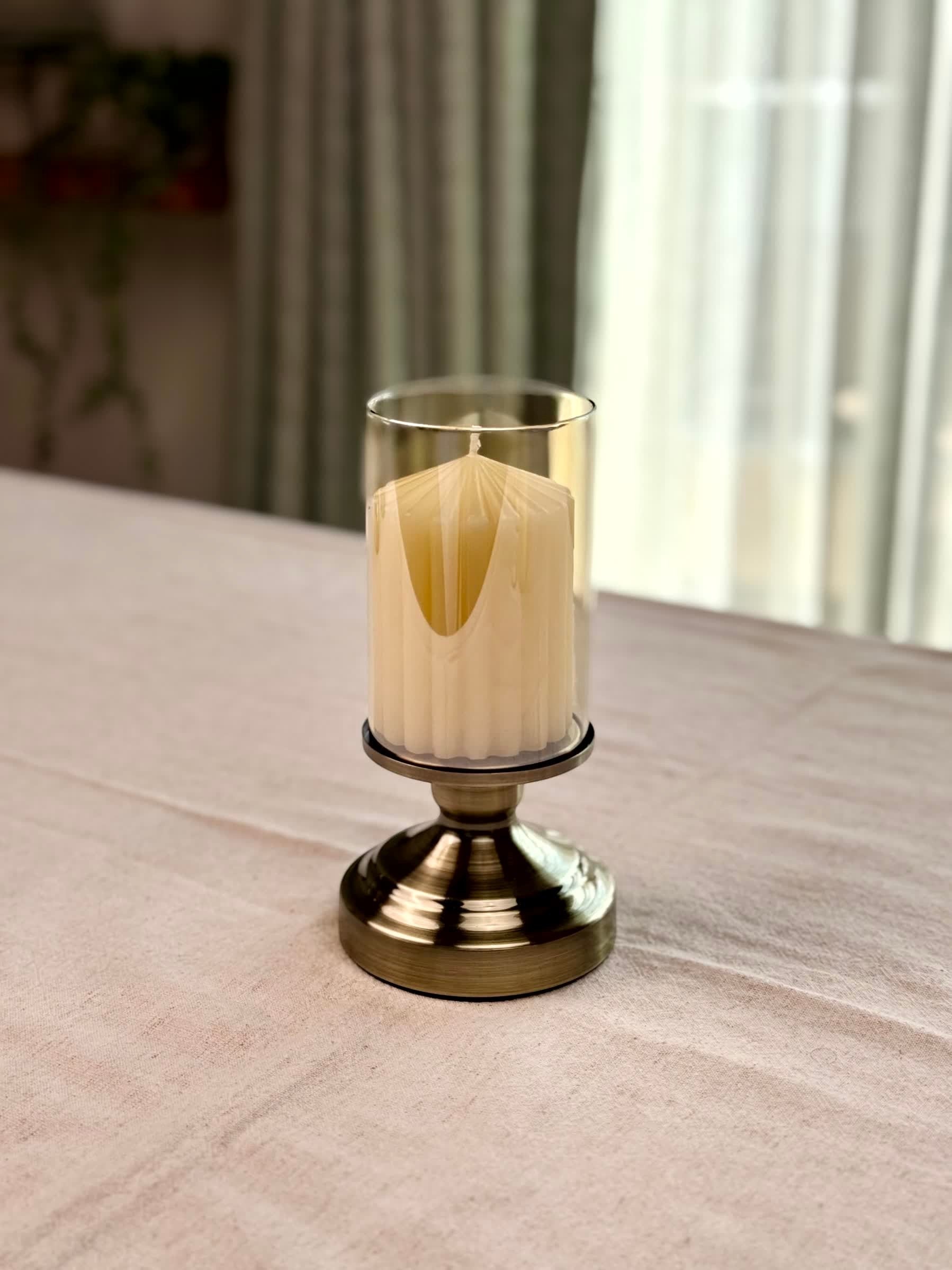 High Objects Luminaria Pedestal Candle Stand Set with tinted glass hurricane and antique brass stem, holding a cream pillar candle.