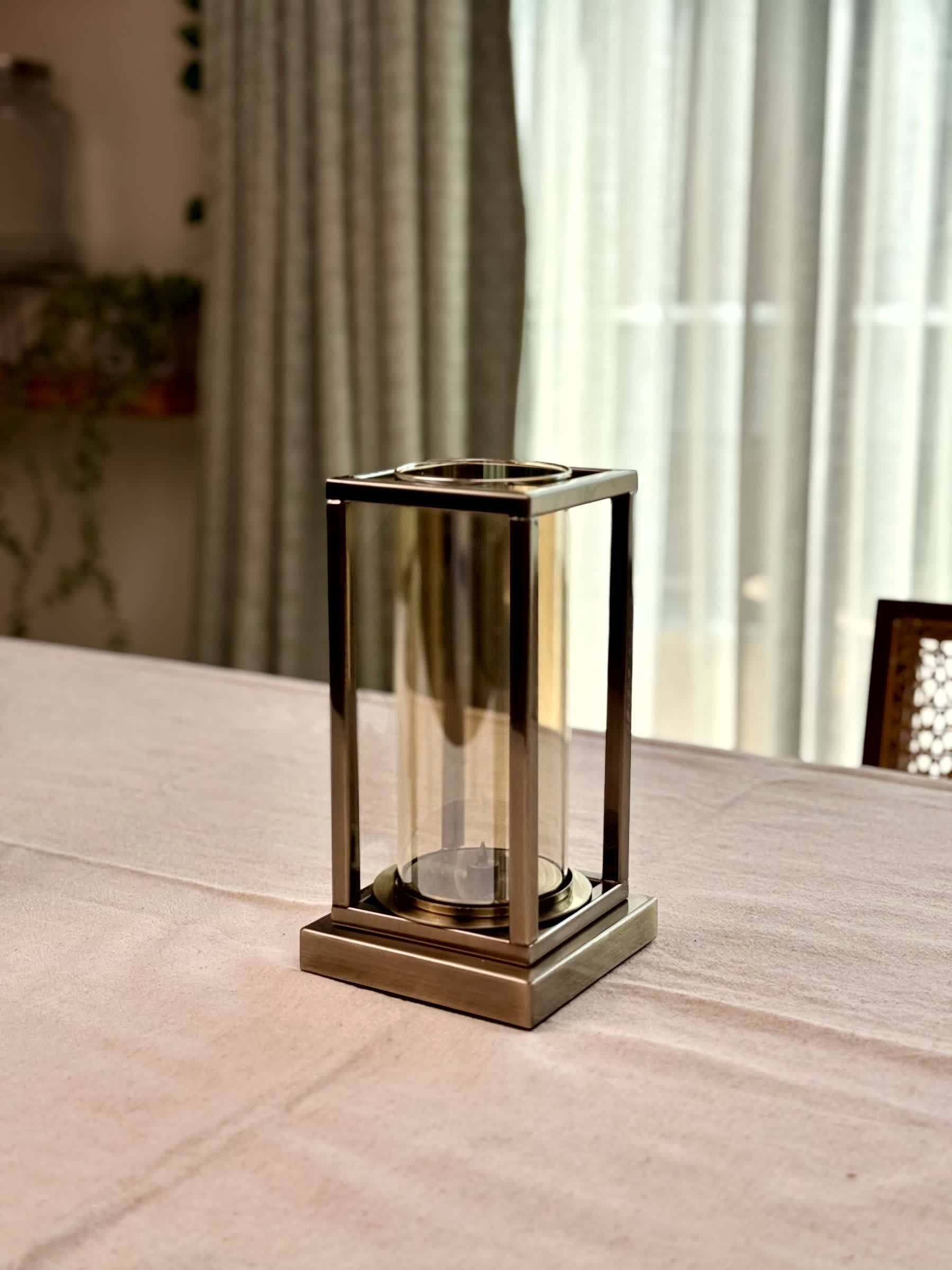 High Objects Modern Halo Frame candle stand with a rectangular metal frame and cylindrical glass chamber, antique brass finish.