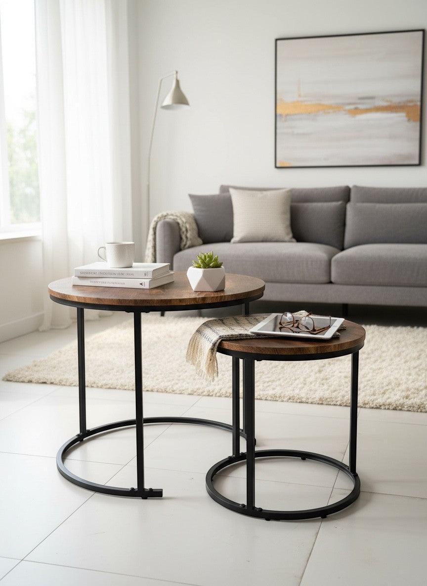 High Objects modern nesting coffee table set with round wooden tops and black metal frames. One table holds books and a plant, the other a tablet and glasses.