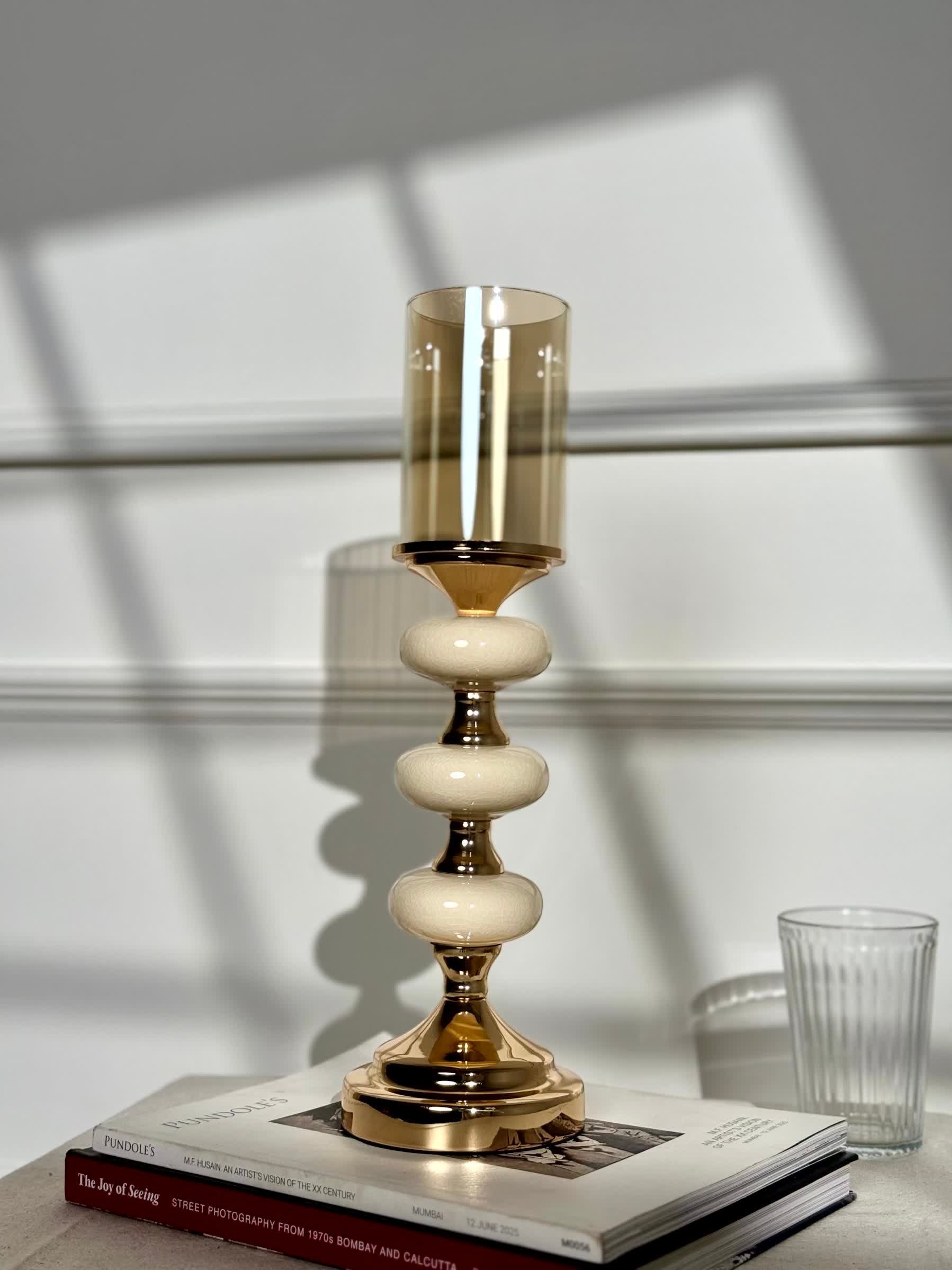 High Objects Pebble Luxe candle stand with gold base, cream pebble accents, and amber glass hurricane.