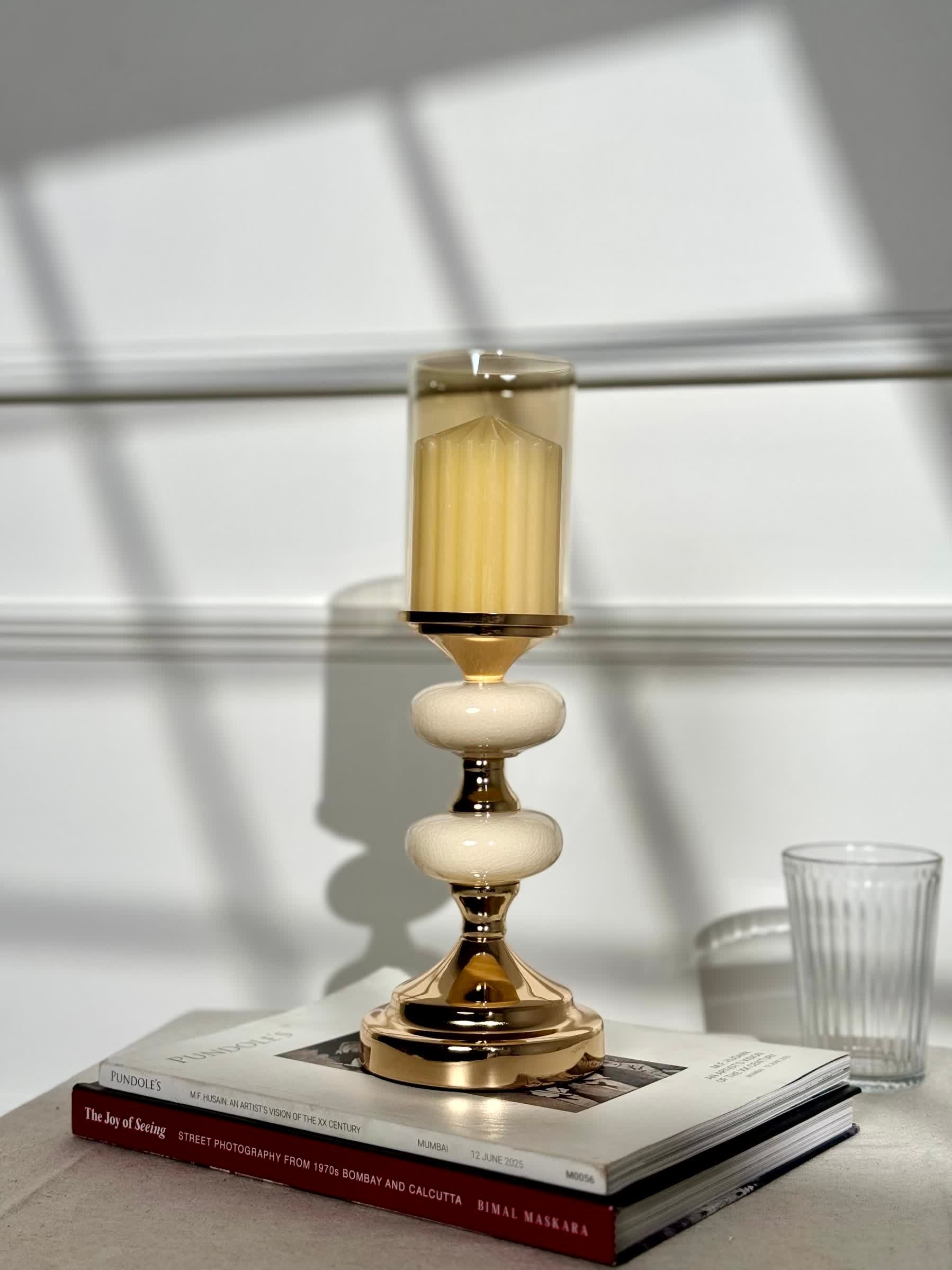 High Objects Pebble Luxe candle stand with gold base, cream pebble-shaped accents, and amber glass hurricane.