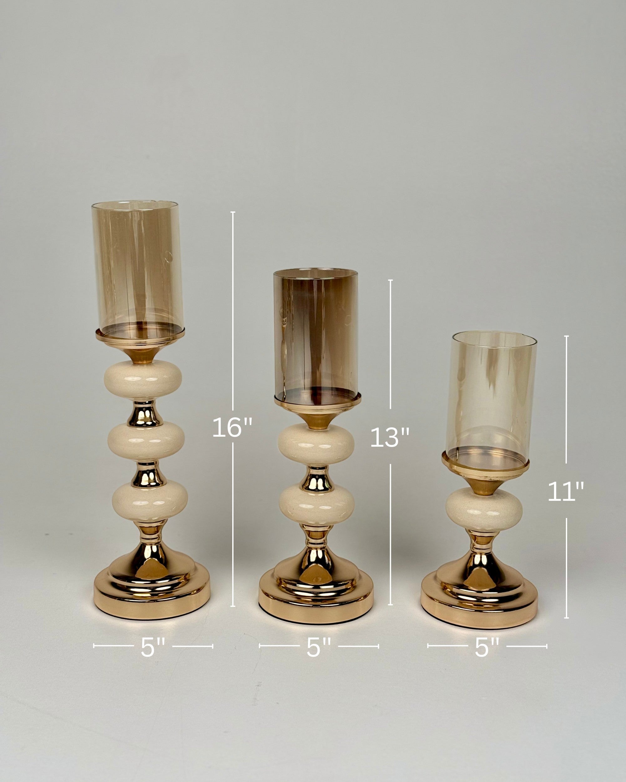 High Objects Pebble Luxe Candle Stand Set, set of 3 gold candle holders with amber glass hurricanes and cream pebble-like stems.