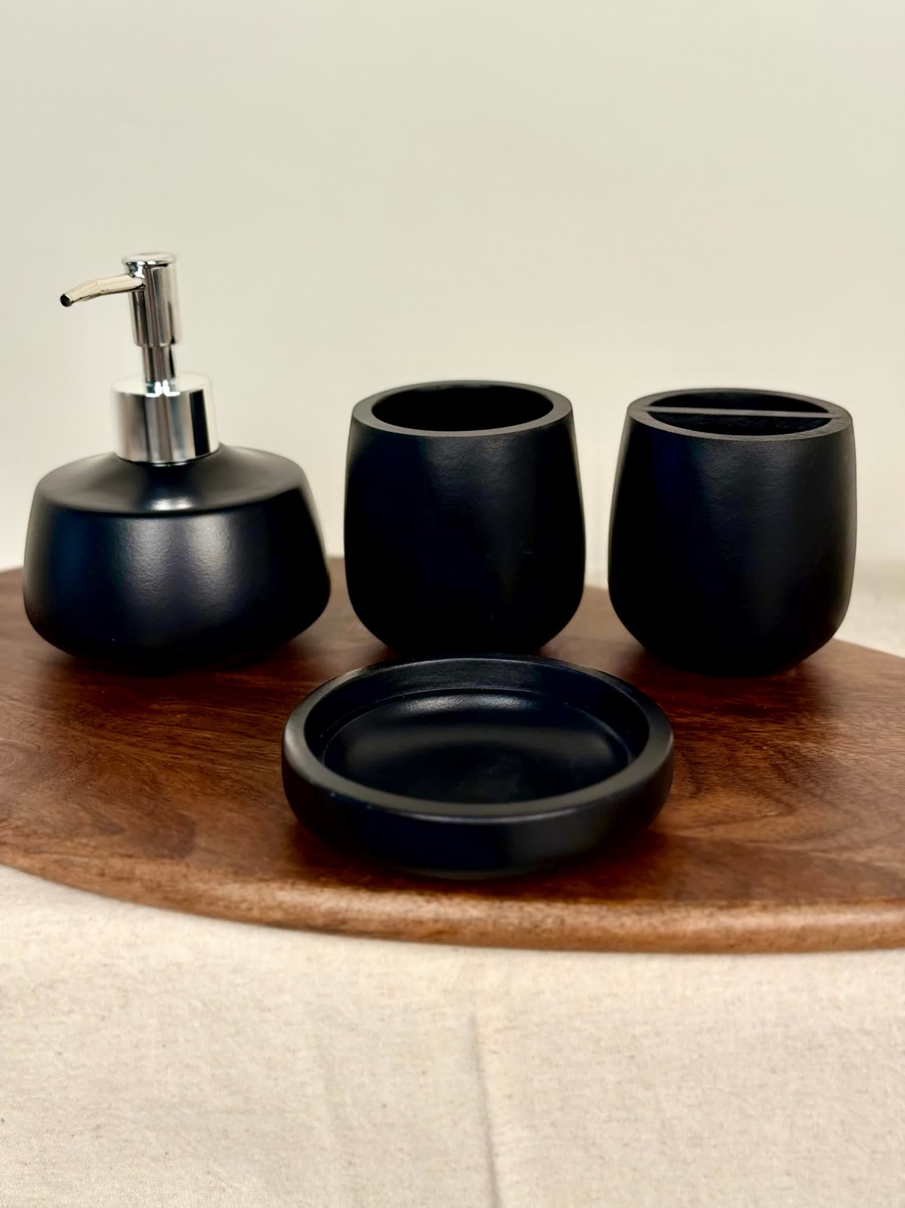 High Objects Pebbleease black bathroom accessory set with soap dispenser, toothbrush holder, and cup on wooden tray.