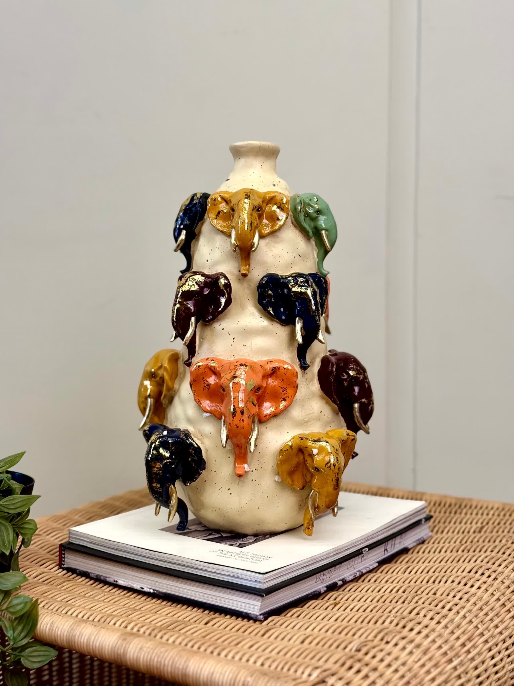 High Objects Safari Heritage Elephant Art Showpiece, a cream ceramic vase with multiple colorful elephant heads and gold tusks.
