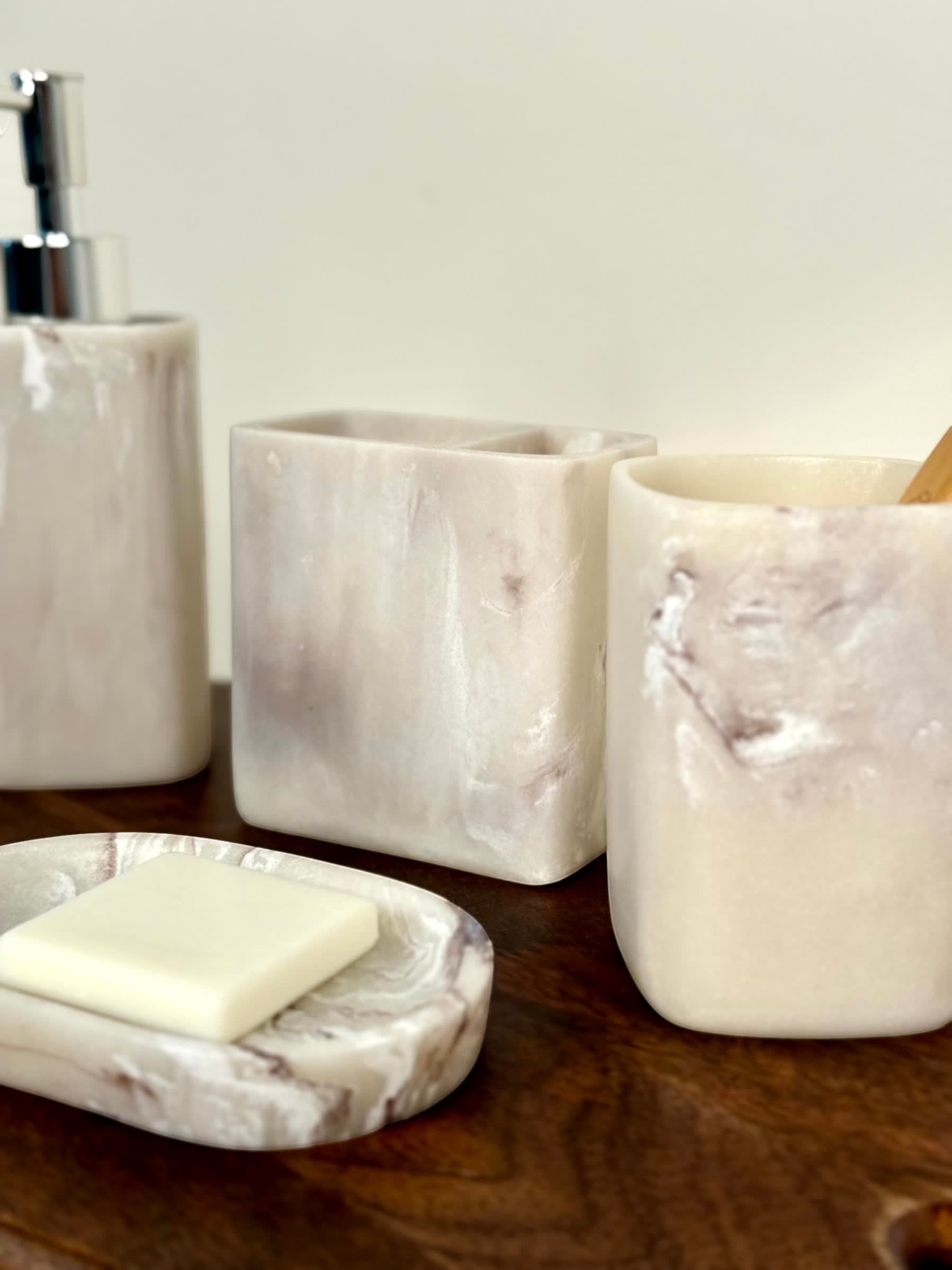 High Objects Stoneaura bathroom accessory set in marbled cream and grey resin, includes soap dish, dispenser, and cups.