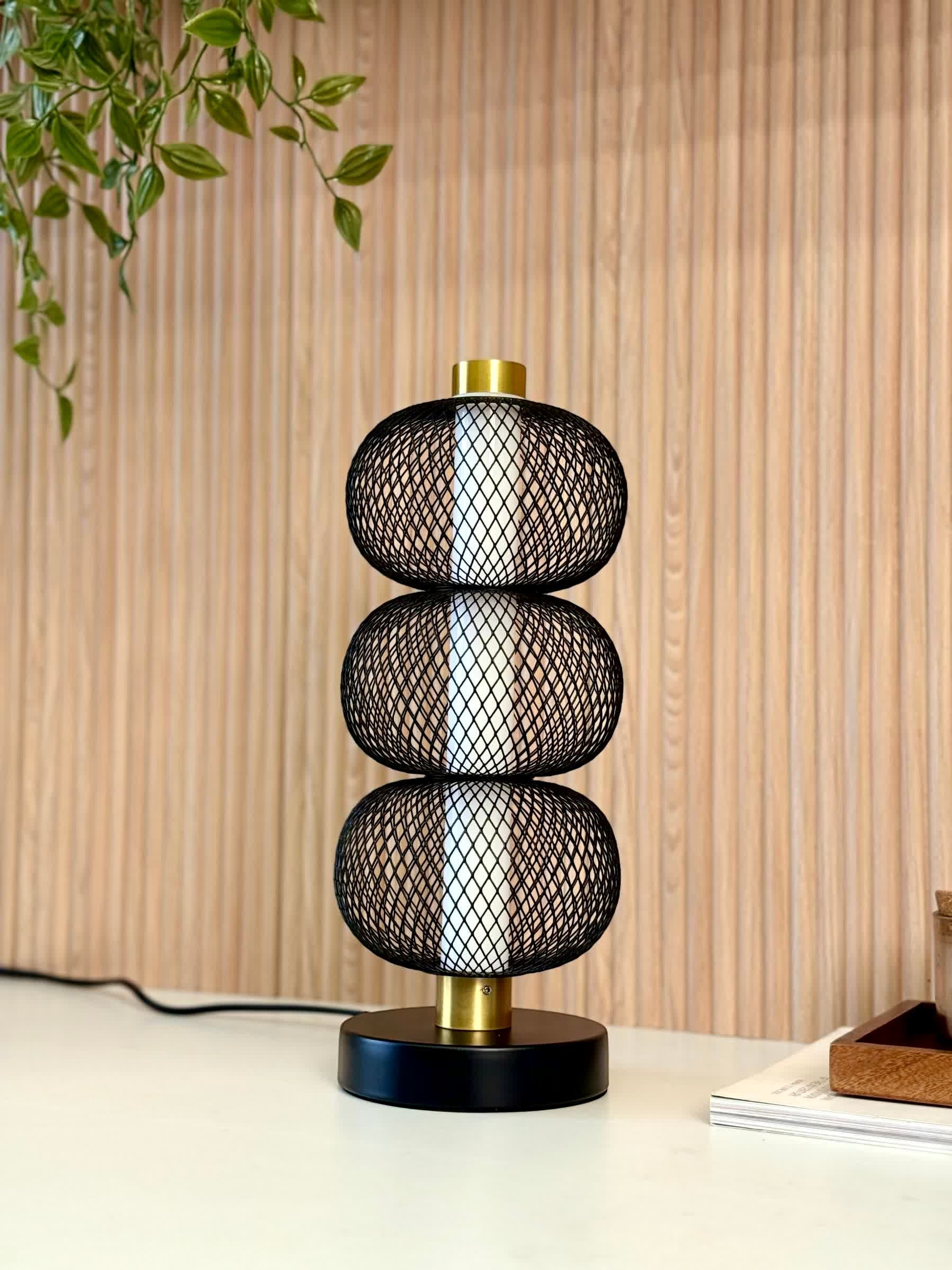 High Objects Trinity Mesh Table Lamp with stacked black lattice spheres and brushed gold accents on a black base.