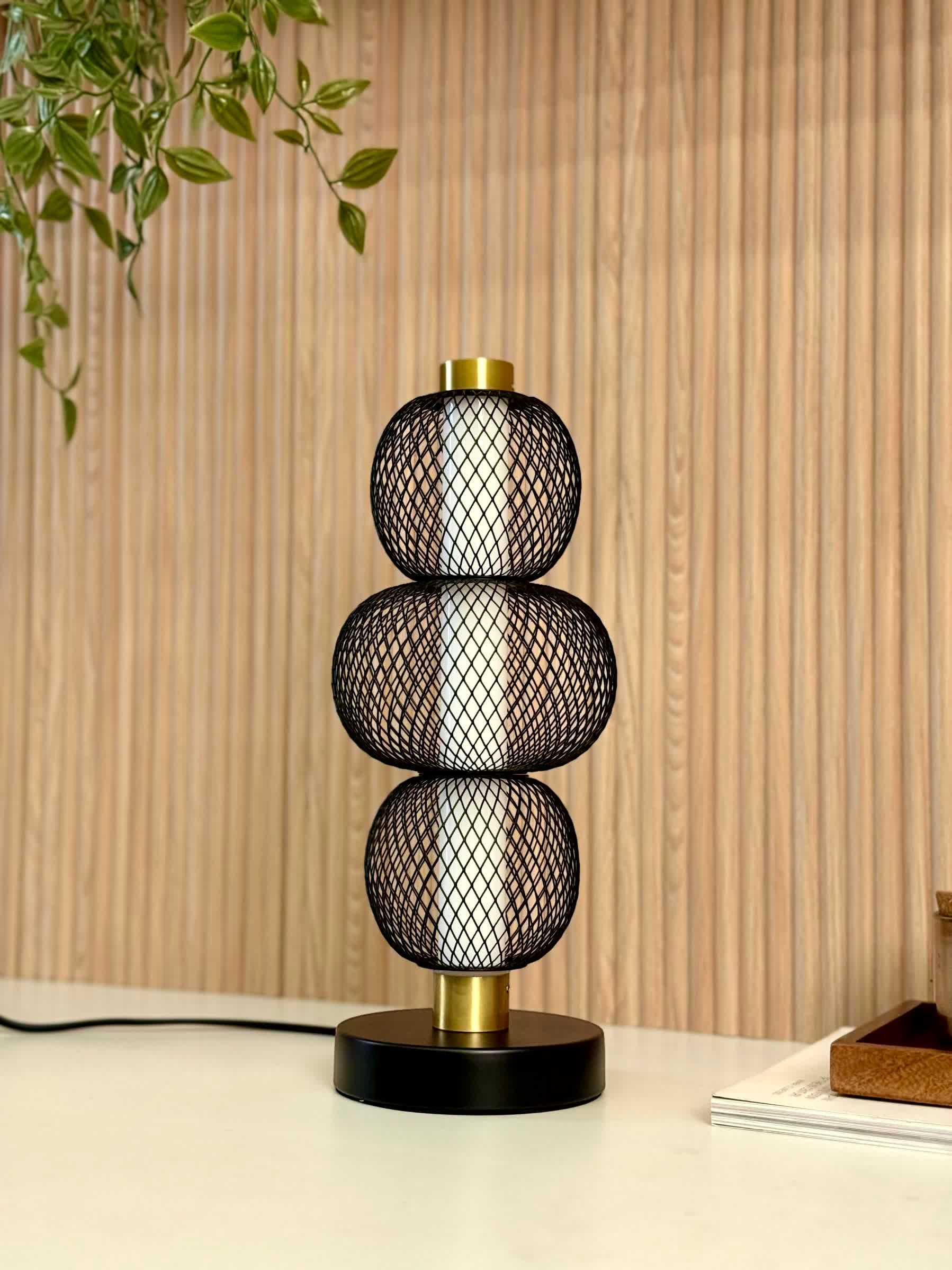 High Objects Trinity Slim Mesh Table Lamp with stacked black mesh spheres and brushed gold accents on a black base.