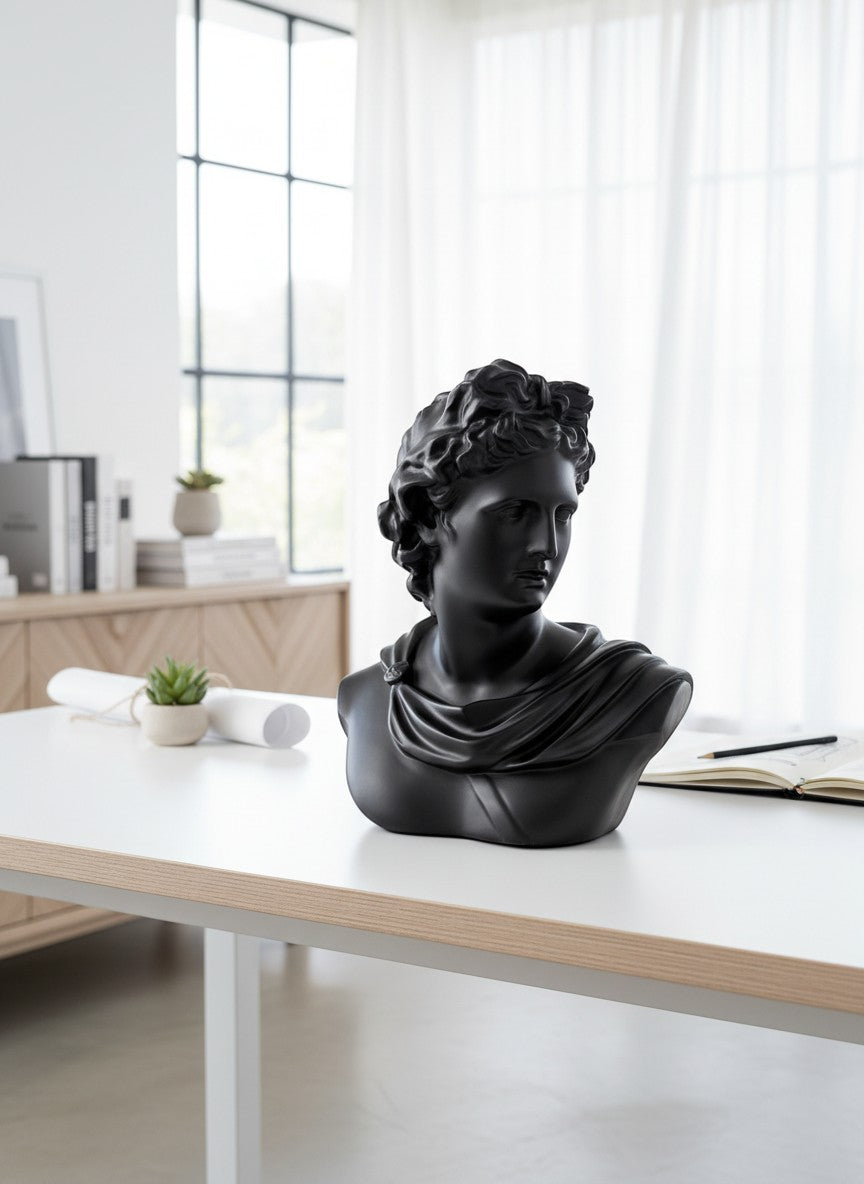 High Objects black matte bust of Apollo, a classical sculpture with intricate hair and draped clothing, displayed on a white desk.