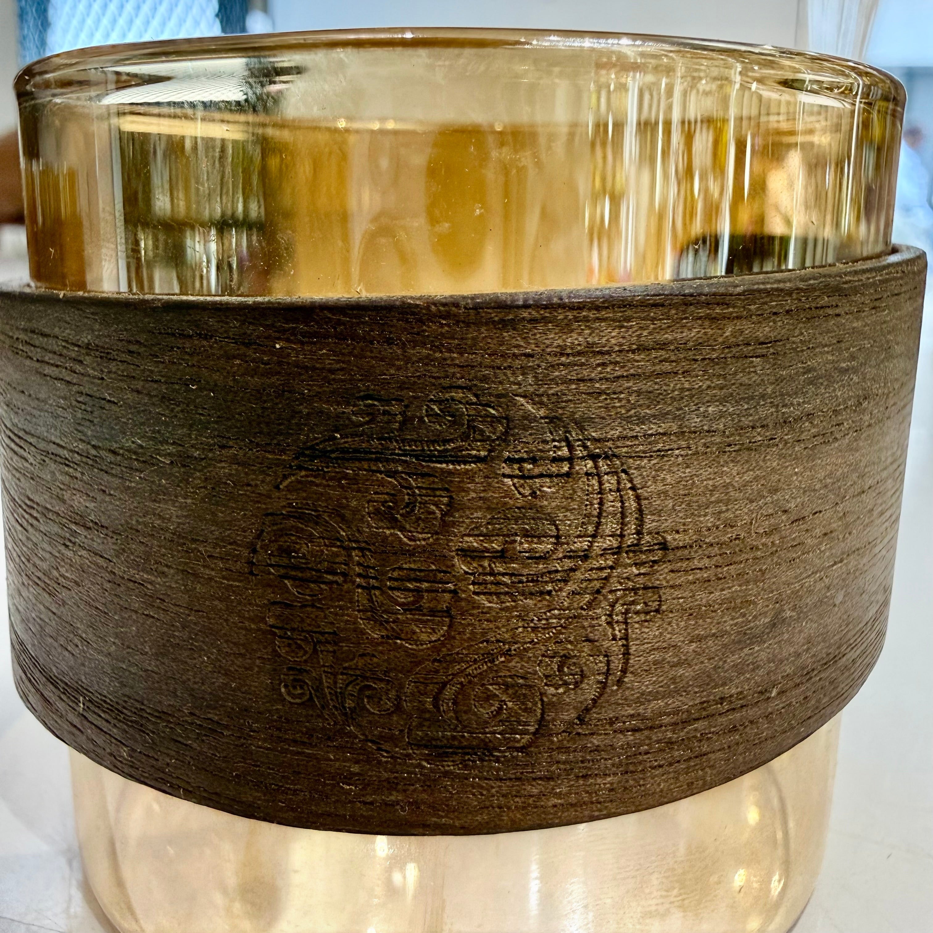 High Objects EMBERFORM glass cup with amber tint and textured wooden sleeve featuring an embossed ornate design.