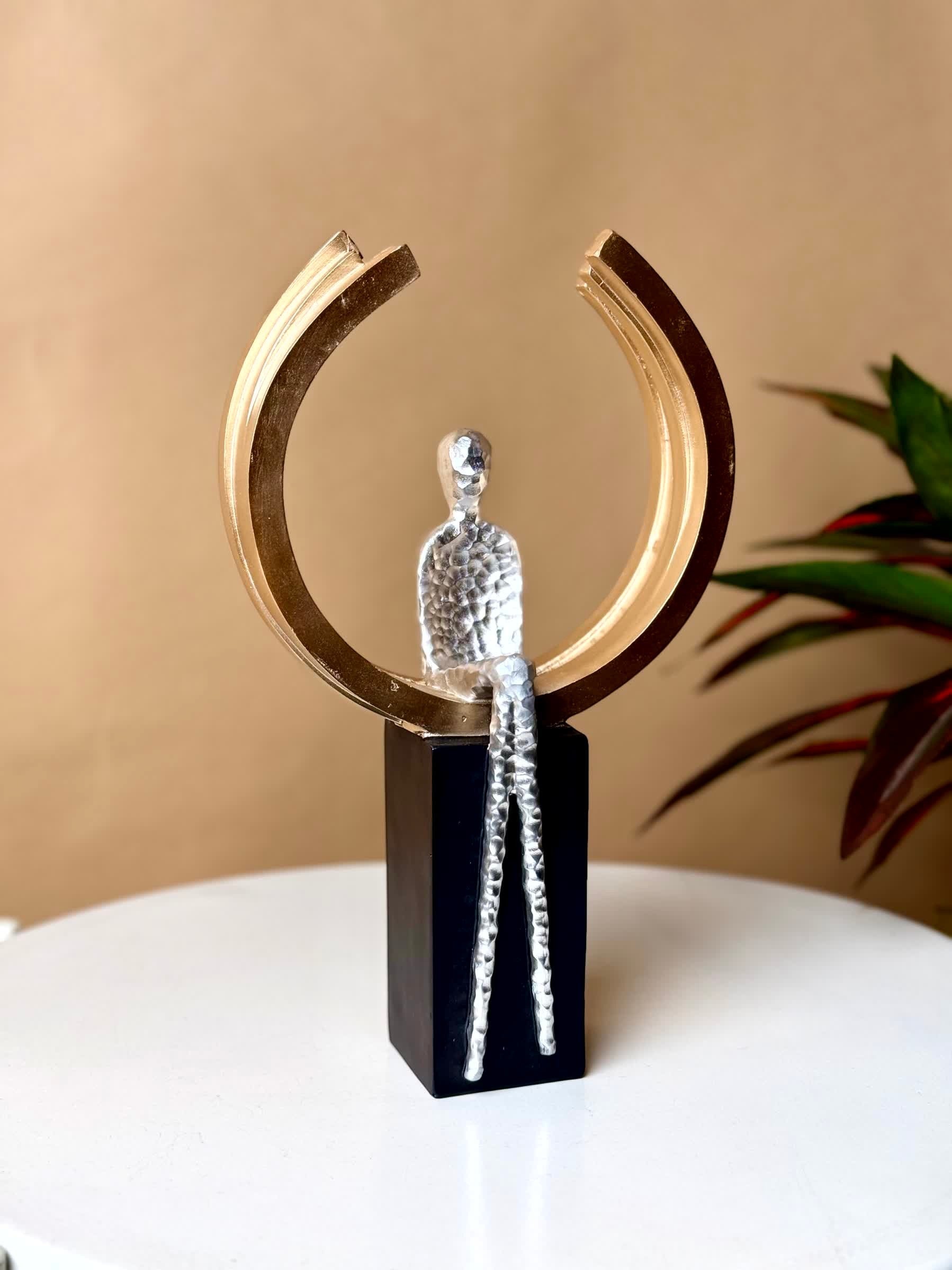 High Objects Arc of Reflection Showpiece: silver hammered figure seated in gold arc on black base. Modern sculpture.