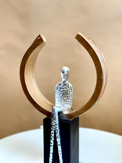 High Objects Arc of Reflection Showpiece, silver hammered figure seated in gold arc on black base, modern art sculpture.