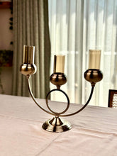 High Objects Circa Arc Triple Candle Stand in antique brass with amber glass holders. Arched design with circular accent.