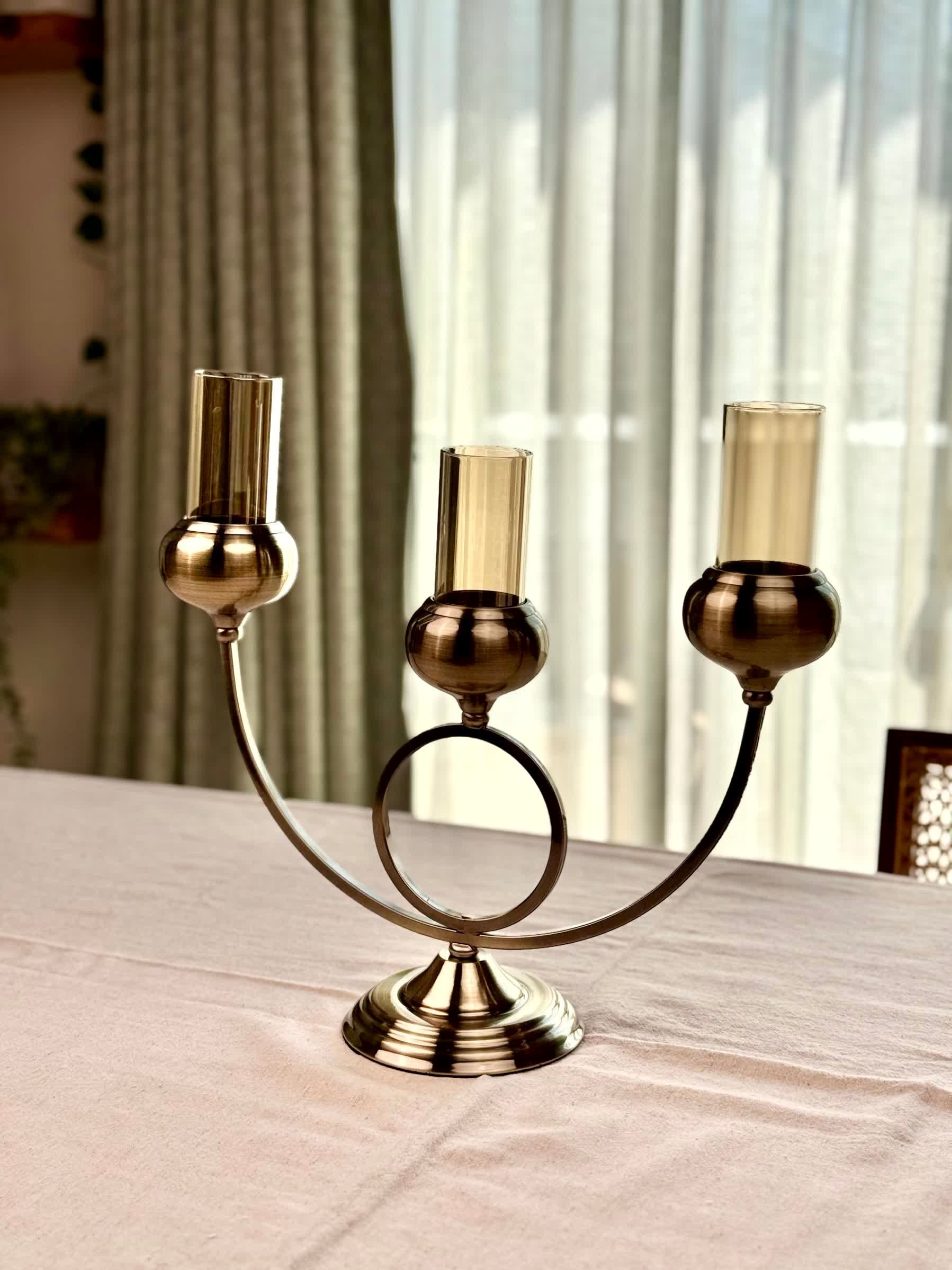High Objects Circa Arc Triple Candle Stand in antique brass with amber glass holders. Arched design with circular accent.