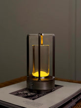 High Objects Aria Frame Table Lamp with clear glass shade and brushed metal base, emits warm yellow light.