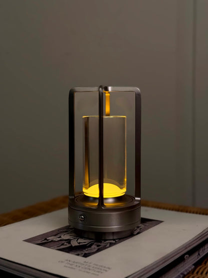 High Objects Aria Frame Table Lamp with clear glass shade and brushed metal base, emits warm yellow light.