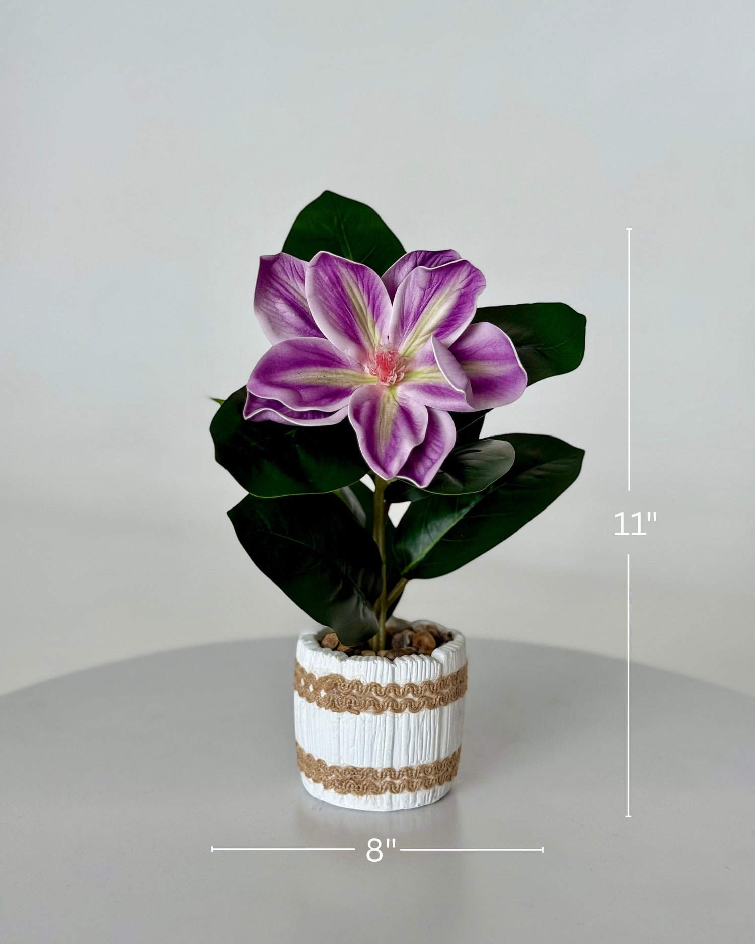 High Objects artificial purple and white lily plant in a white striped ceramic pot with pebbles. 11" H x 8" W.