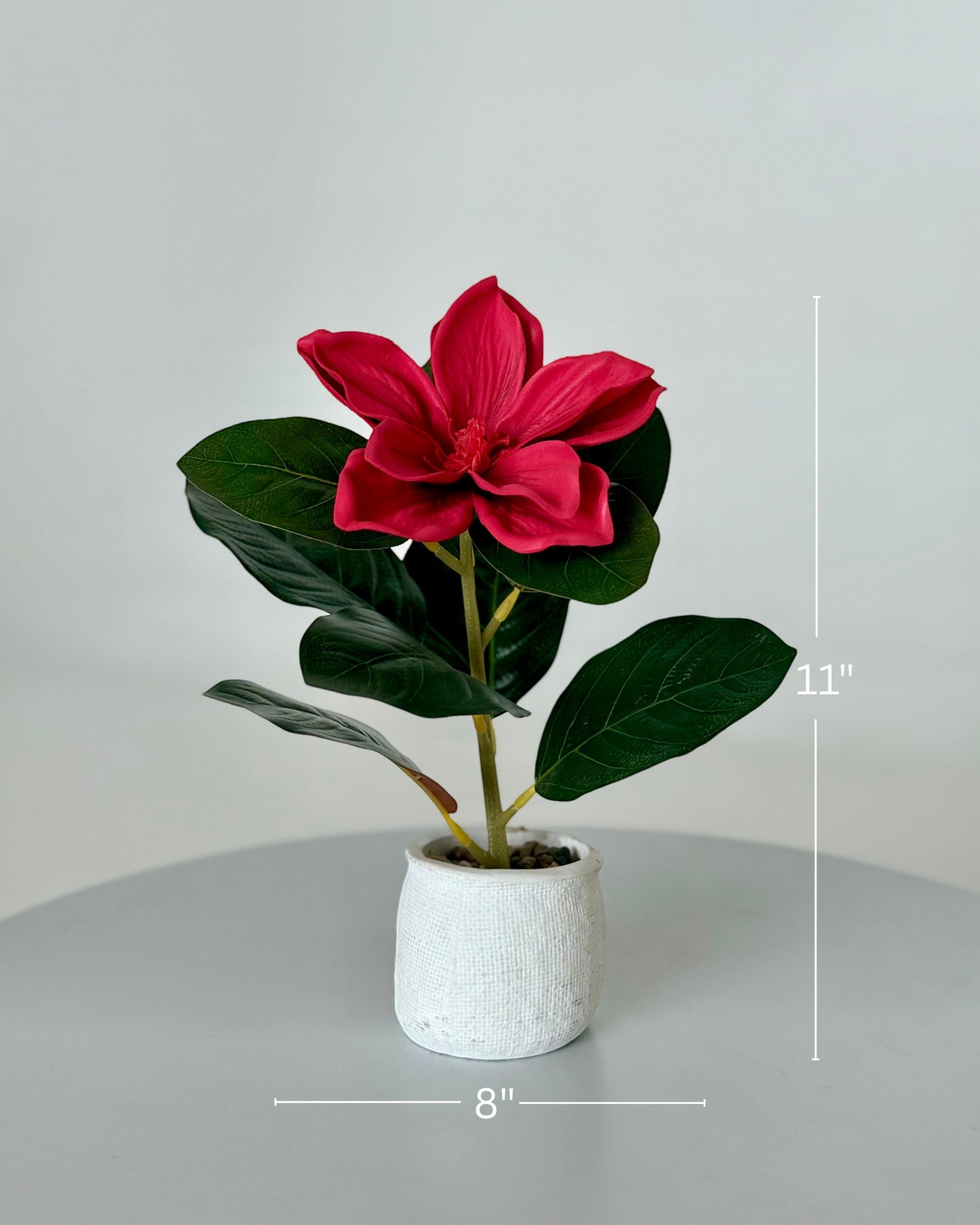 High Objects red artificial lily plant with lush green leaves in a textured white ceramic pot with pebbles. 11" H x 8" W.