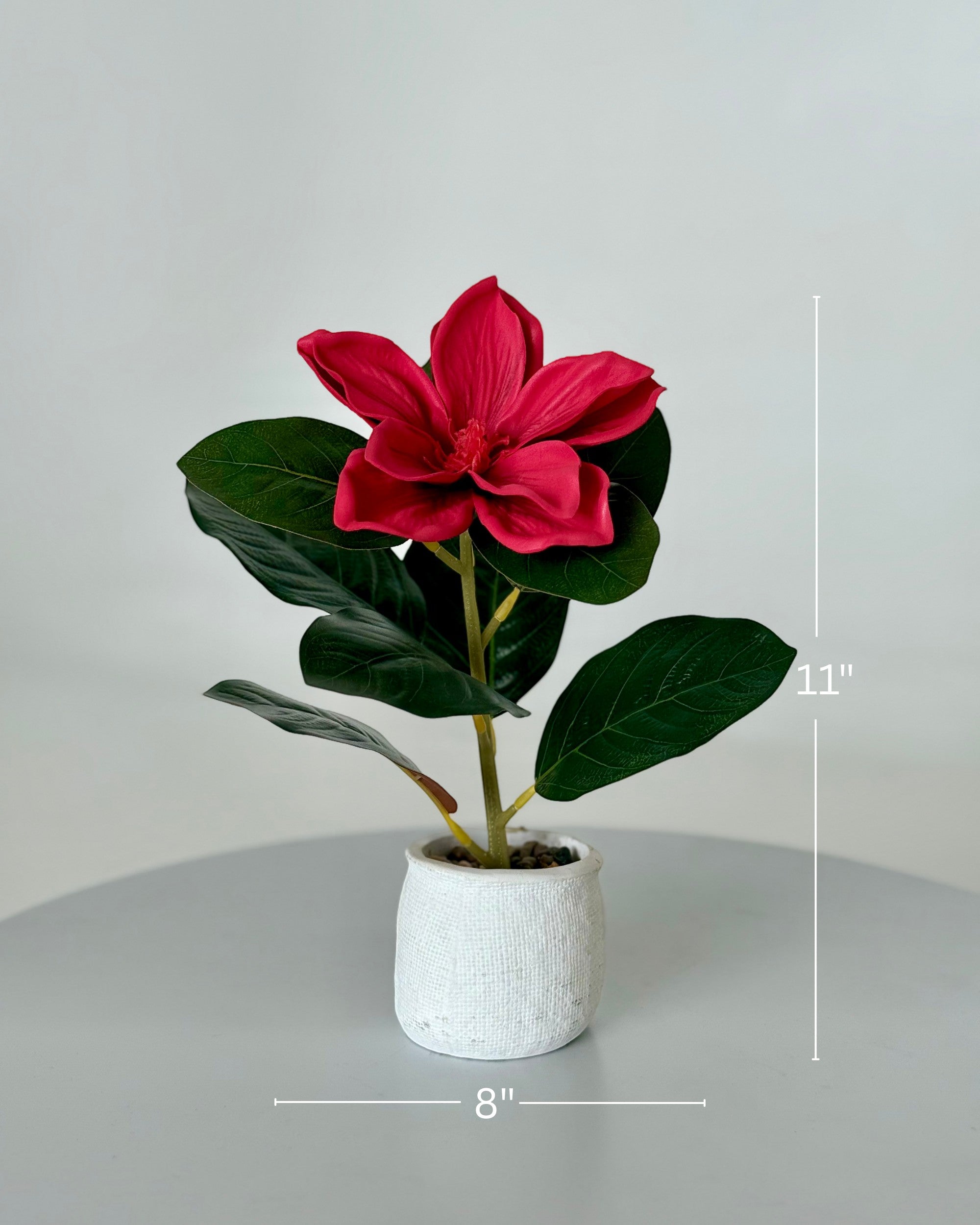 High Objects red artificial lily plant with lush green leaves in a textured white ceramic pot with pebbles. 11" H x 8" W.