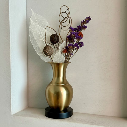 High Objects Aurelia Vase: brushed gold metallic vase with black base, featuring dried flowers and decorative leaves.