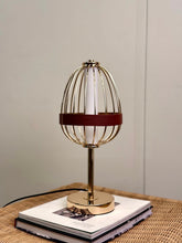High Objects Aurette Cage Table Lamp with gold wire cage, leather band, and gold base. Modern sculptural design.