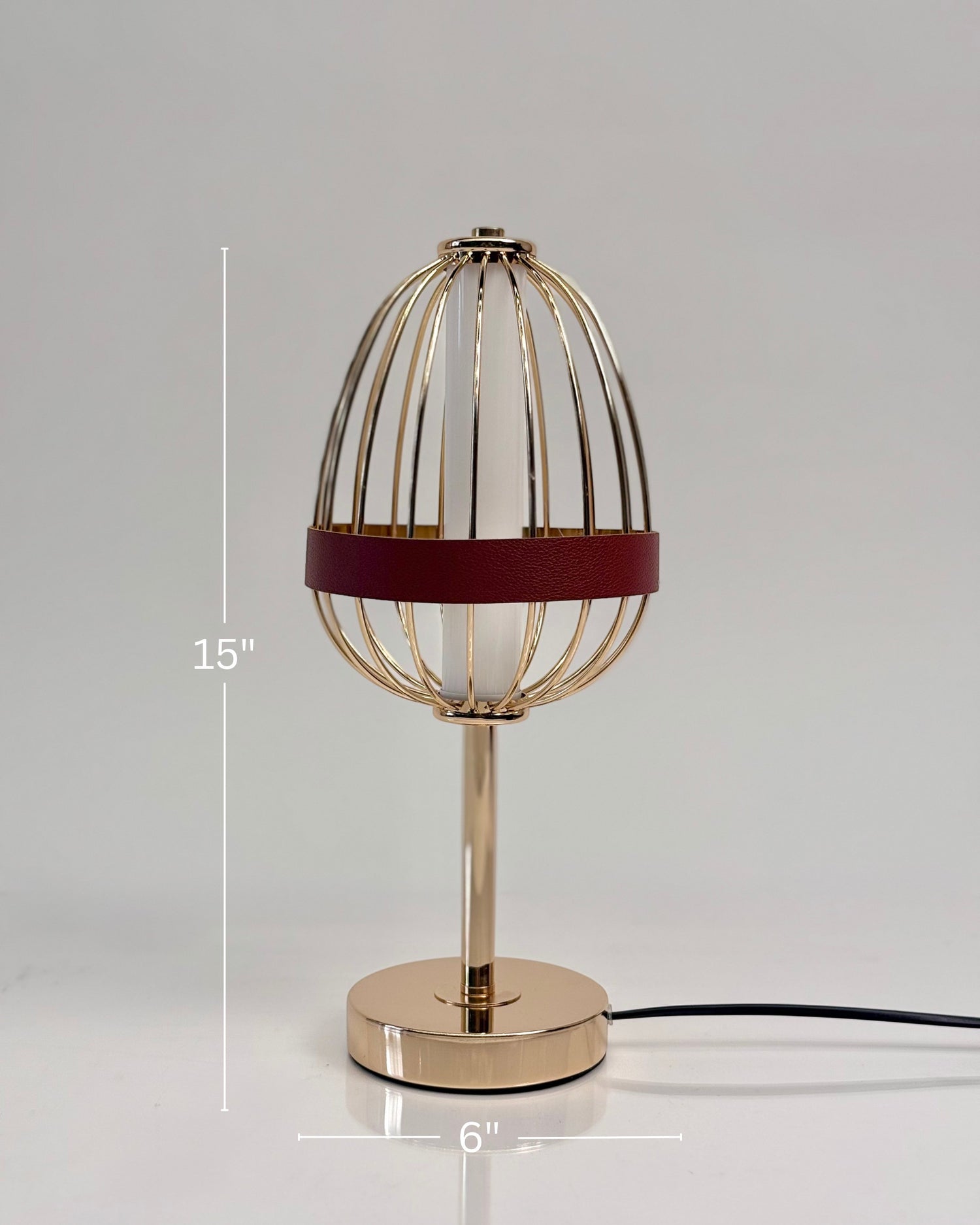 High Objects Aurette Cage Table Lamp: Gold wire cage with red leather band surrounds a white candle-shaped bulb. Sleek gold base.