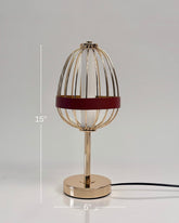 High Objects Aurette Cage Table Lamp: Gold wire cage with red leather band surrounds a white candle-shaped bulb. Sleek gold base.