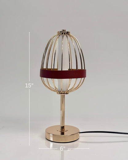 High Objects Aurette Cage Table Lamp: Gold wire cage with red leather band surrounds a white candle-shaped bulb. Sleek gold base.