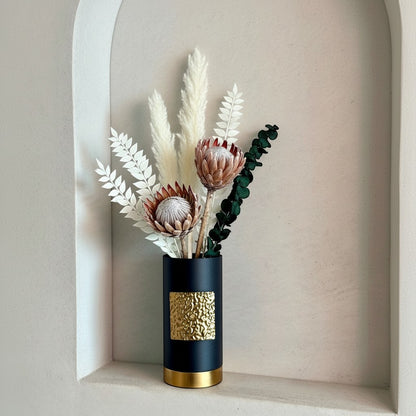 High Objects Aurum Noir matte black cylindrical vase with textured gold band and base, holding dried flowers.