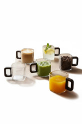High Objects AXISFORM™ set of 6 square glass cups with geometric handles, some filled with coffee, matcha, juice, and water.