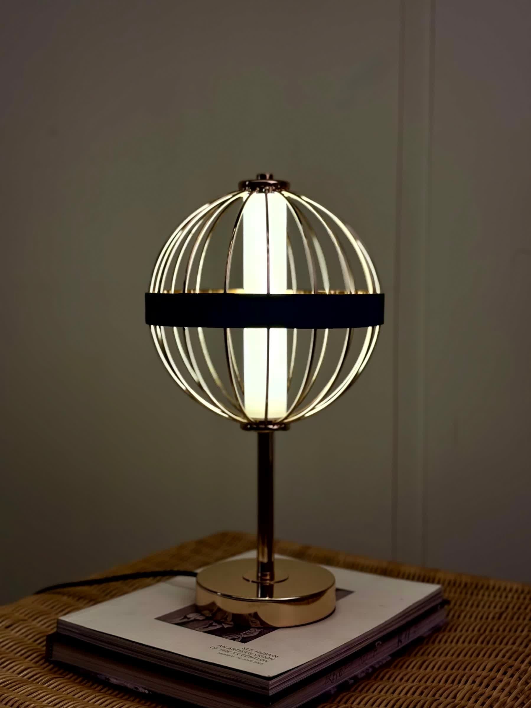 High Objects Azure Aurette Cage Table Lamp with gold wire globe, blue leather band, and gold stem on a stack of books.