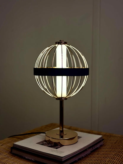 High Objects Azure Aurette Cage Table Lamp with gold wire globe, blue leather band, and gold stem on a stack of books.