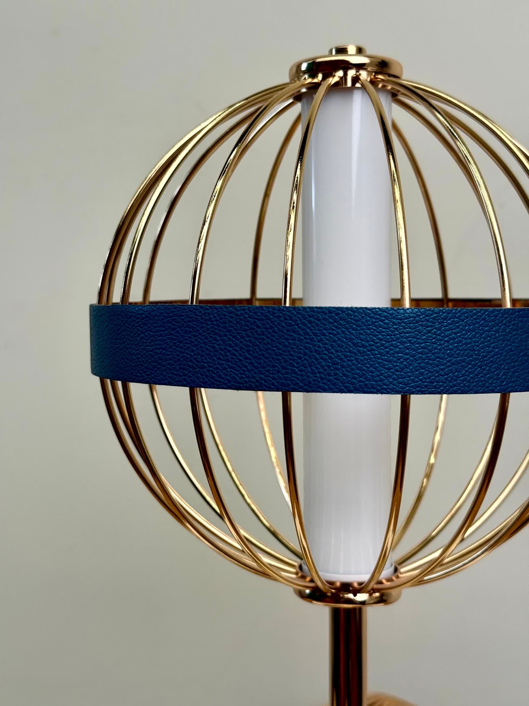 High Objects Azure Aurette table lamp with gold wire cage, white cylinder shade, and blue leather accent band.