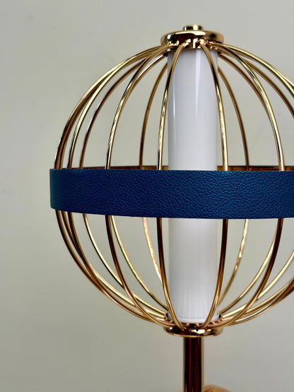High Objects Azure Aurette table lamp with gold wire cage, white cylinder shade, and blue leather accent band.