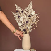 High Objects beige ceramic vase with wavy rim, holding dried eucalyptus and pampas grass. Hand with gold watch.