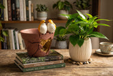 High Objects decorative terracotta-style planter with two yellow bird figurines perched on a stack of interior books