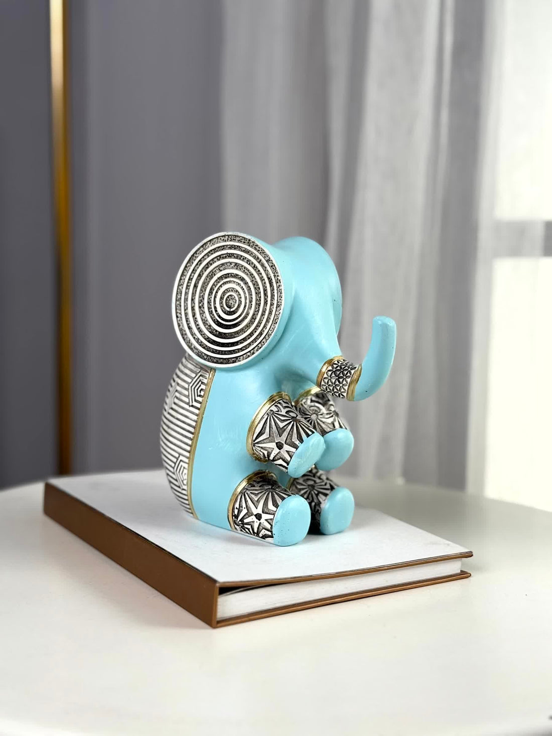 High Objects small blue polyresin elephant figurine with geometric black and white patterns and gold accents, sitting on a book.