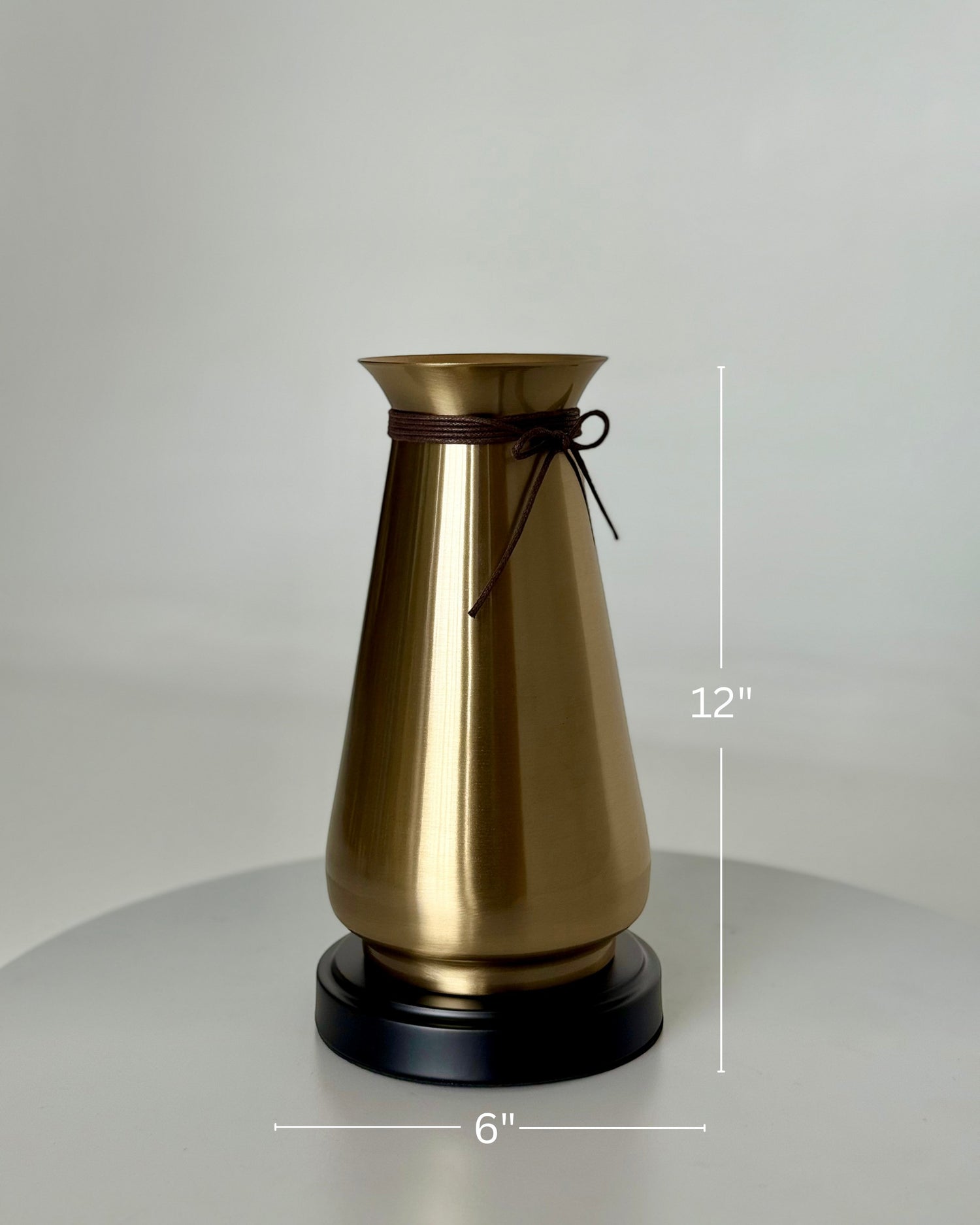 High Objects Celestia Vase, a gold tapered vase with a flared rim and cord detail, on a black base.