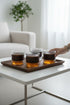 High Objects CINDER set of 4 amber textured glass cups with dark matte sleeves on a wooden tray.