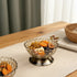 High Objects Crystal Bloom Accent Bowl, a textured glass bowl with scalloped rim on a metallic pedestal base, filled with dried fruits and nuts.