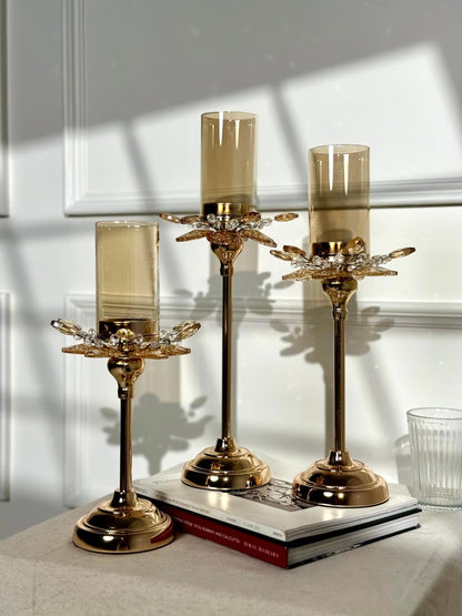High Objects set of 3 gold candle stands with amber glass hurricanes and crystal petal accents. Elegant floral design.