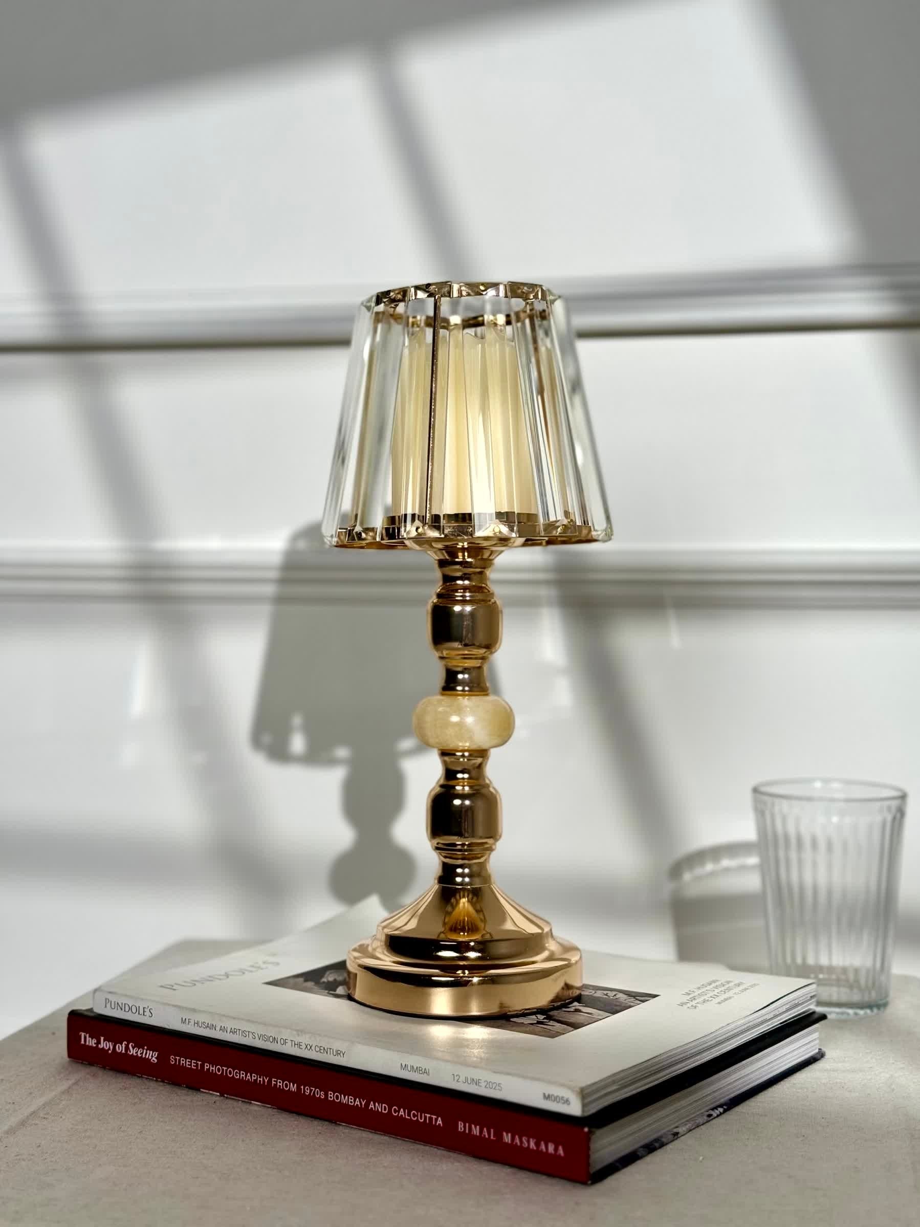 High Objects Crystal Belle candle stand with faceted glass shade and gold pedestal stem, on books.