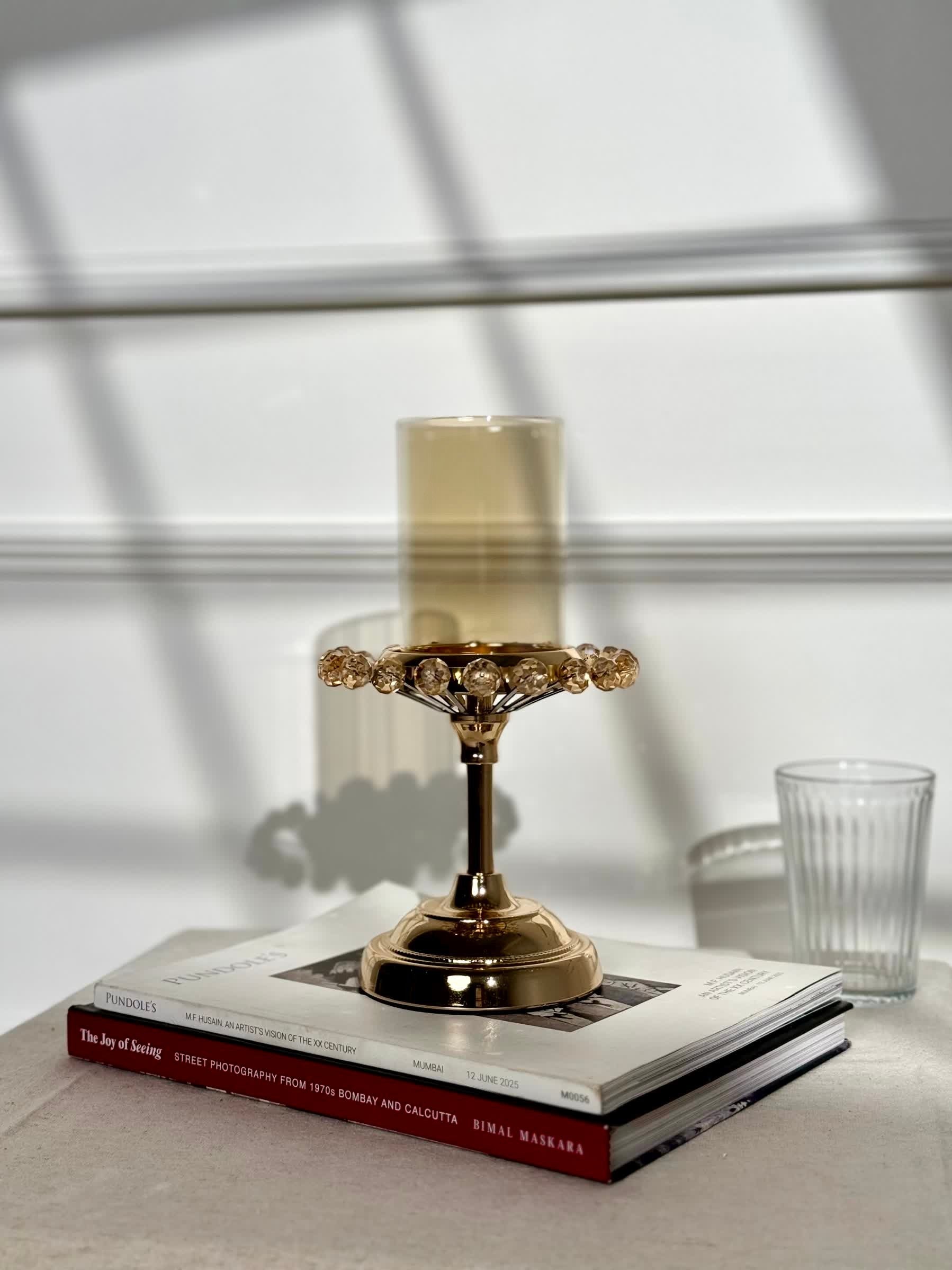 High Objects gold candle stand with crystal halo detail and pedestal base, on stacked books.