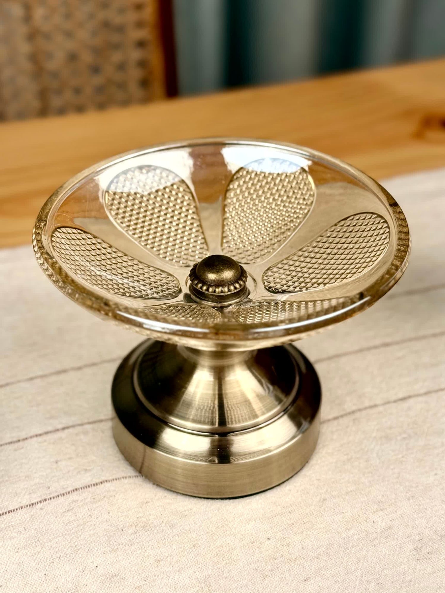 High Objects clear glass pedestal platter with petal-shaped rim and textured surface. Antique brass base.