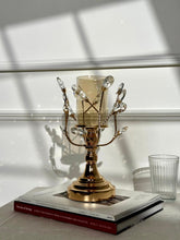 High Objects gold metal candle stand with crystal leaves and amber glass hurricane on books.