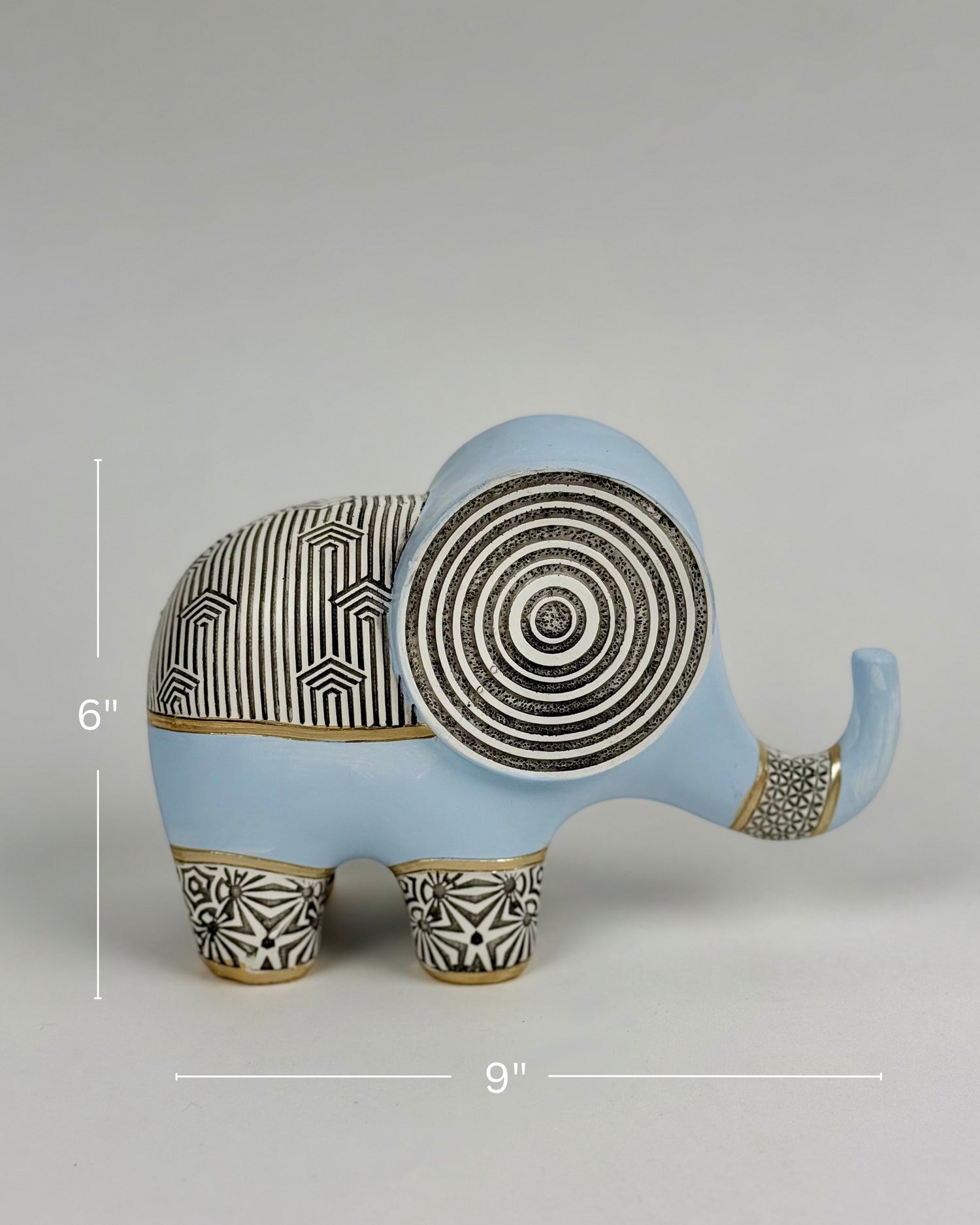 High Objects Elysian Trunk Figurine, a soft blue polyresin elephant with black and gold geometric patterns on its body and ears.